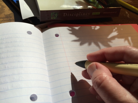 Photo of a hand poised over paper with a pen - with stark shadows on the paper. Books and a highlighter can be seen in the upper part of the photo.