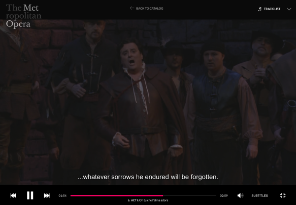 Image shows a screenshot of a scene in a production of the Metropolitan Opera. A man sings, with a group of other men standing behind him. The subtitles read, "...whatever sorrows he endured will be forgotten."